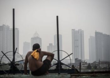 Seorang warga berjemur dengan latar belakang gedung bertingkat tersamar kabut polusi udara di Jakarta, Selasa (20/4/2021).