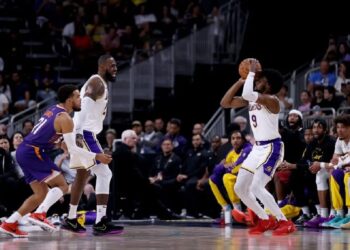 Pemain rookie Los Angeles Lakers, Bronny James (kanan), berupaya melakukan tembakan tiga angka usai diberikan umpan dari ayahnya, LeBron James (kedua kiri), dalam pertandingan melawan Phoenix Suns di laga pramusim NBA.