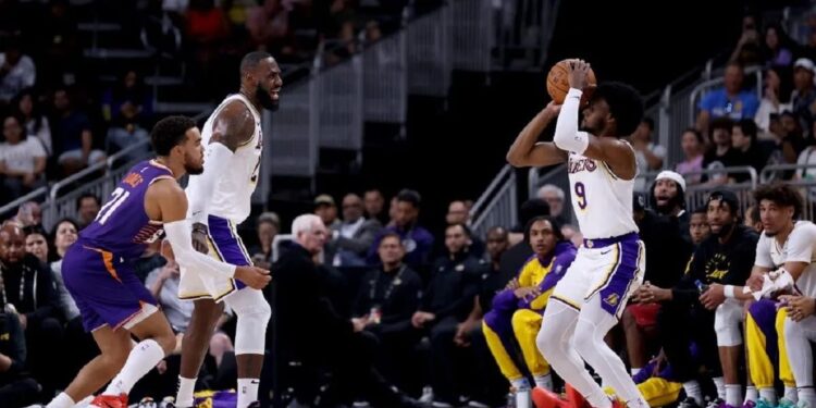 Bermain Bersama di NBA, LeBron dan Bronny James Ukir Sejarah 1 Pemain rookie Los Angeles Lakers, Bronny James (kanan), berupaya melakukan tembakan tiga angka usai diberikan umpan dari ayahnya, LeBron James (kedua kiri), dalam pertandingan melawan Phoenix Suns di laga pramusim NBA.